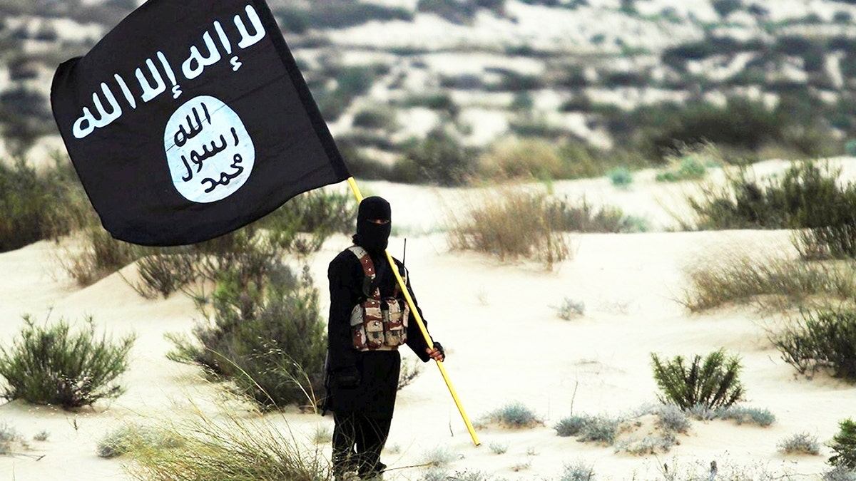 Masked ISIS fighter holds flag in desert