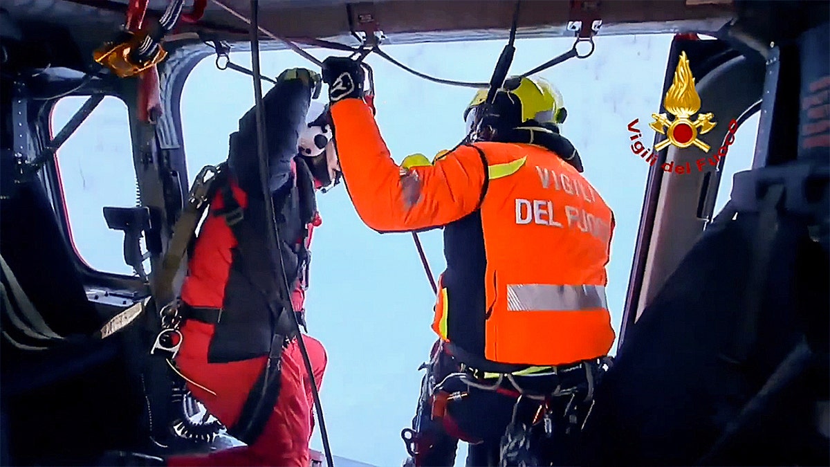 Two Vigili del Fuoco crew members inside a helicopter near an open door.