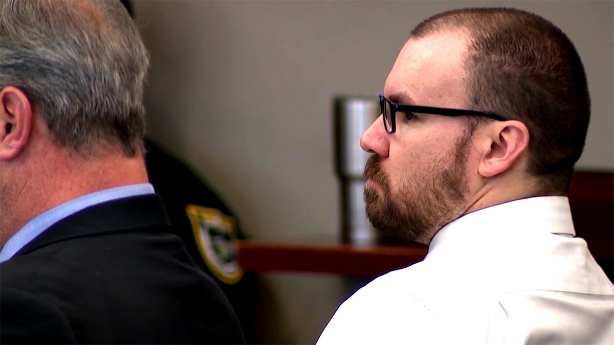 James Melady siedzi w sądzie w okularach i koszuli z kołnierzykiem