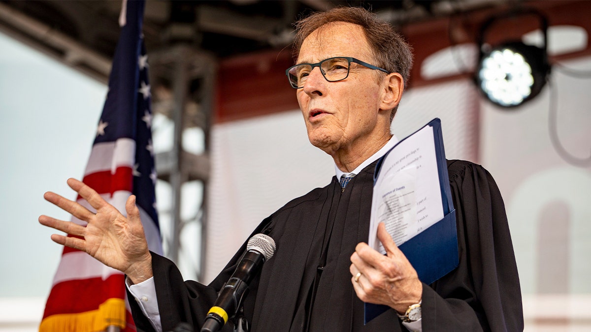 A federal judge addresses newly sworn-in U.S. citizens during an outdoor naturalization ceremony on a public holiday.