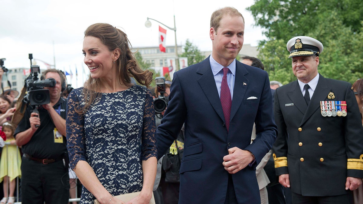 A young Prince William and Kate Middleton walking together outdoors during a royal engagement.