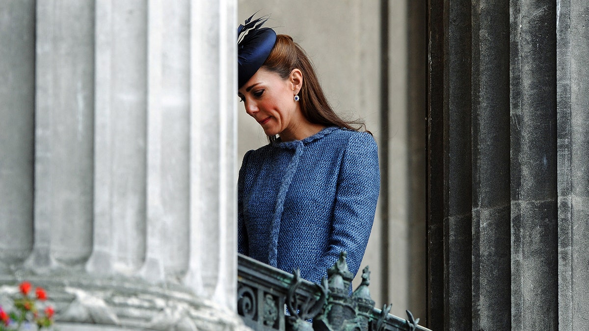 Kate Middleton looking down in a blue dress.