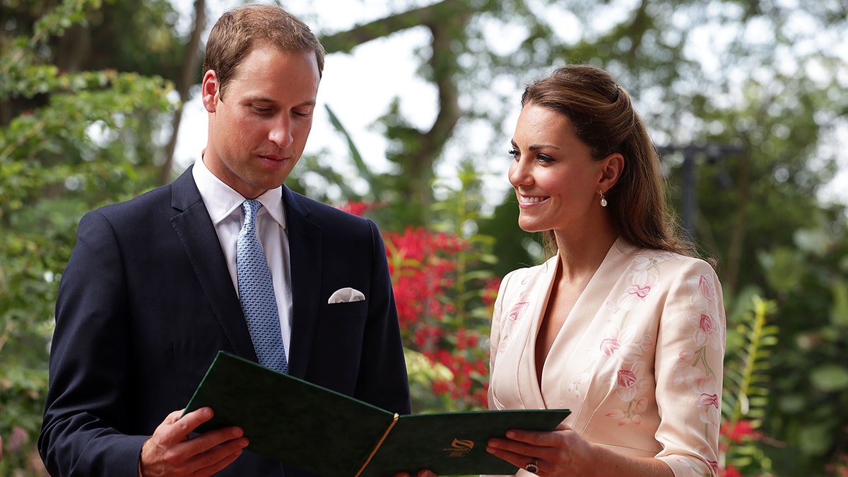 Kate Middleton smiling and holding a folder for Prince William to read.