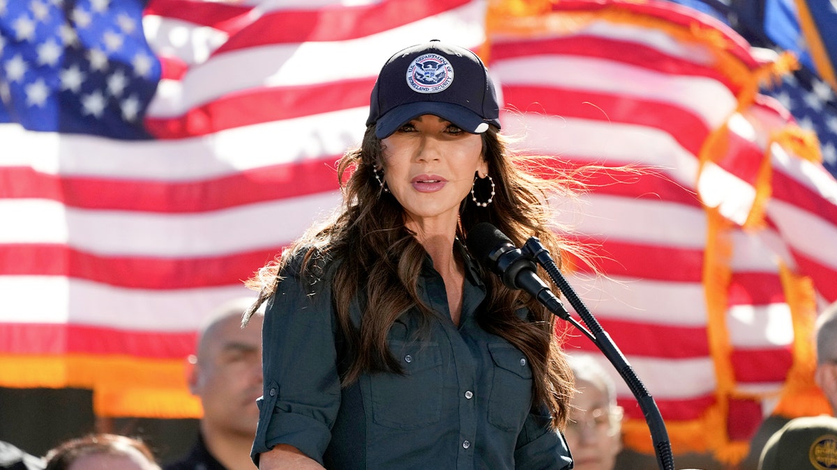 Kristi Noem stoi przed amerykańskimi flagami