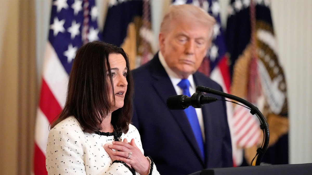 Una donna parla sul podio nella Sala Est della Casa Bianca mentre il presidente Donald Trump guarda.