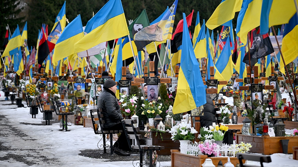 Zwiedzający stoją wśród rzędów świeżych grobów oznaczonych ukraińskimi flagami na Cmentarzu Łyczakowskim we Lwowie.