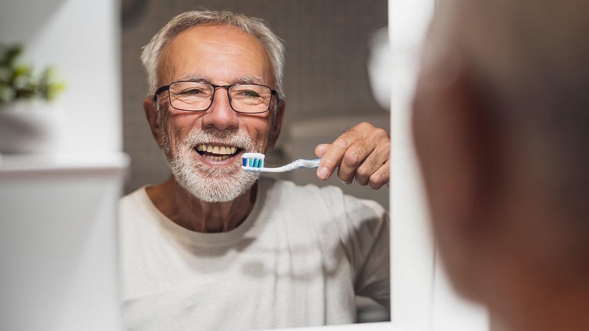 senior man smiles into mirror before brushing teeth