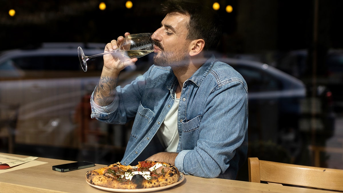 Young mid adult male sitting in a cafe alone while eating pizza and having glass of good wine