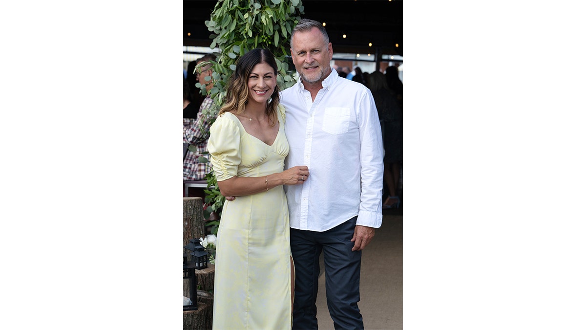 Dave Coulier's wife stands next to him with her arms resting on the actor