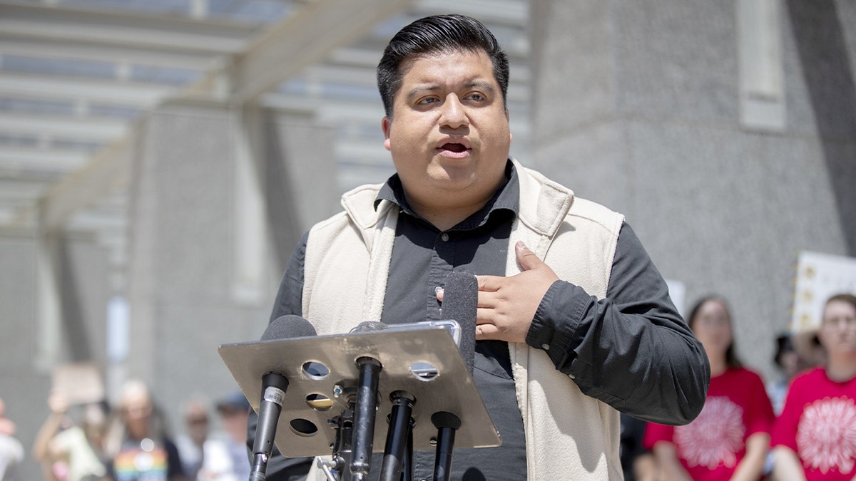 A local elected official speaks at a microphone during an immigration rights protest outside a federal building.