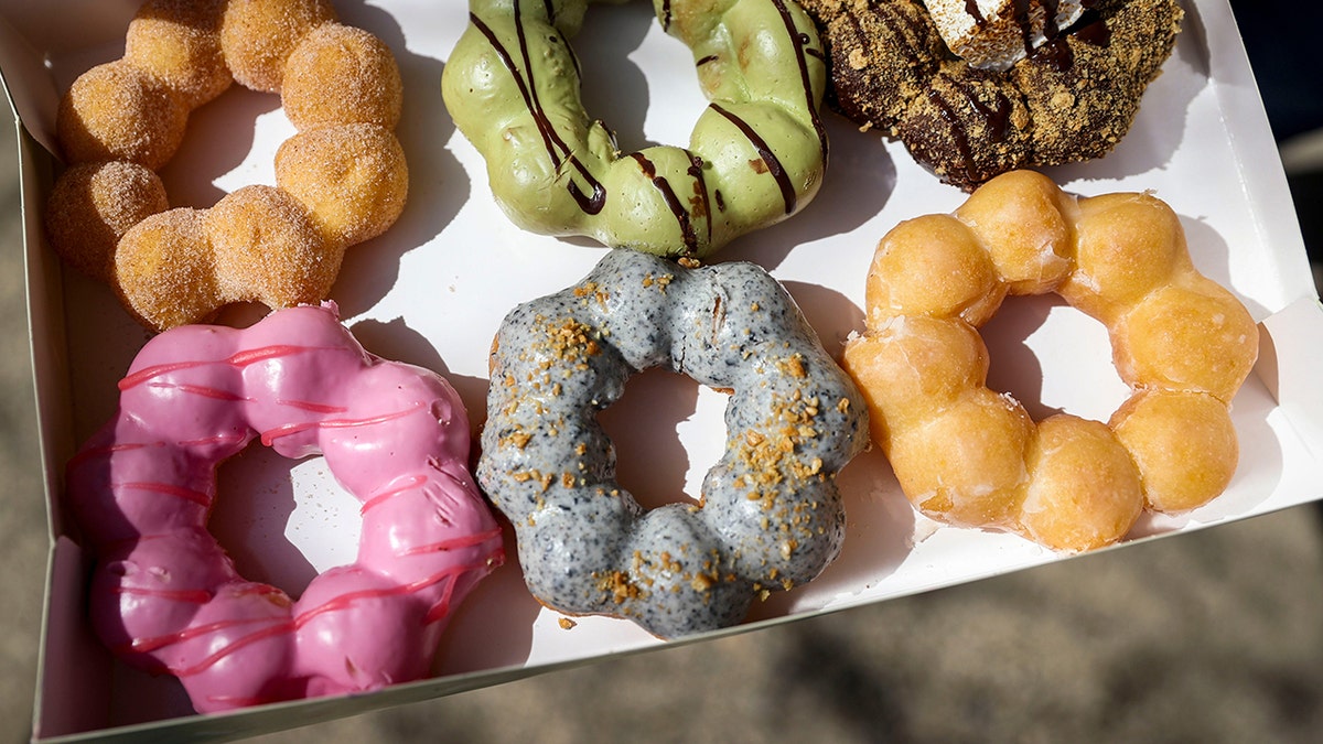 A variety of colorful, fun mochi donuts including cinnamon sugar, matcha, s’more, strawberry, black sesame flavors and glazed in half dozen box.