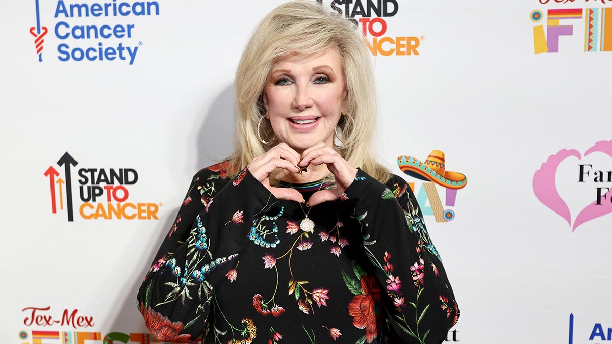 Morgan Fairchild crea il simbolo del cuore con le mani sul tappeto rosso.