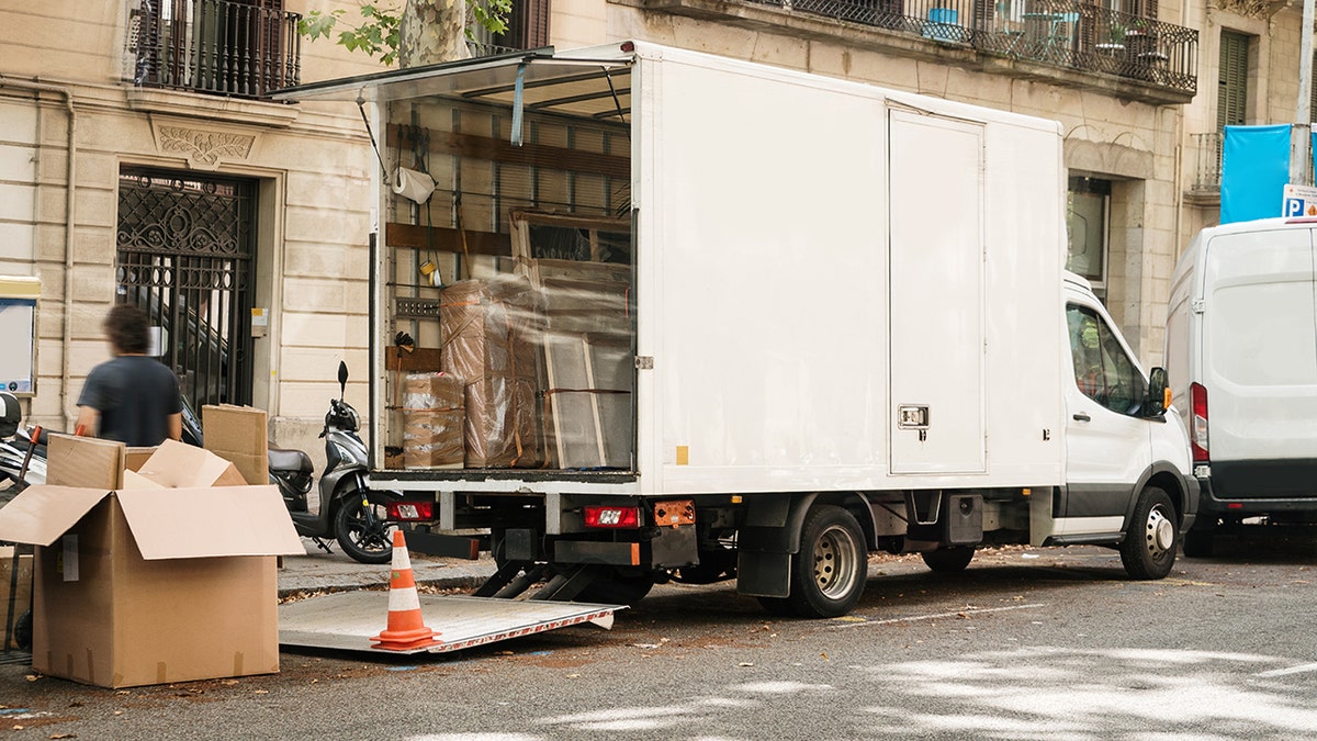Moving truck parked on a city street with its back open, filled with wrapped furniture and boxes during a residential move.