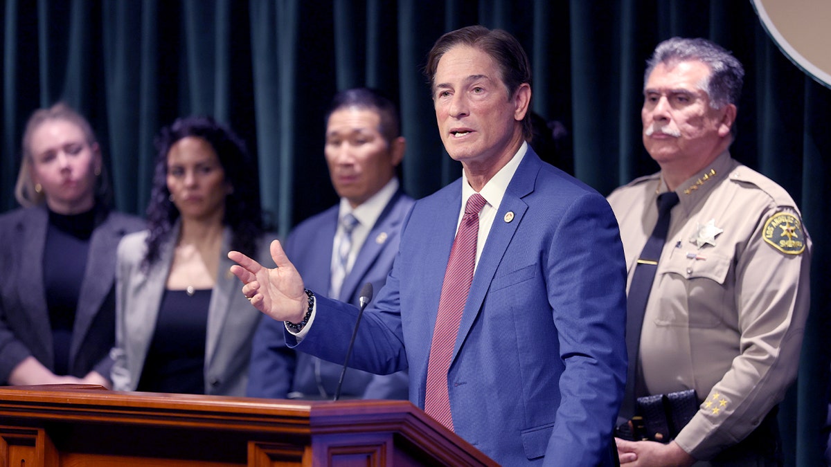 Law enforcement leaders stand at a podium during a public announcement inside a government building.