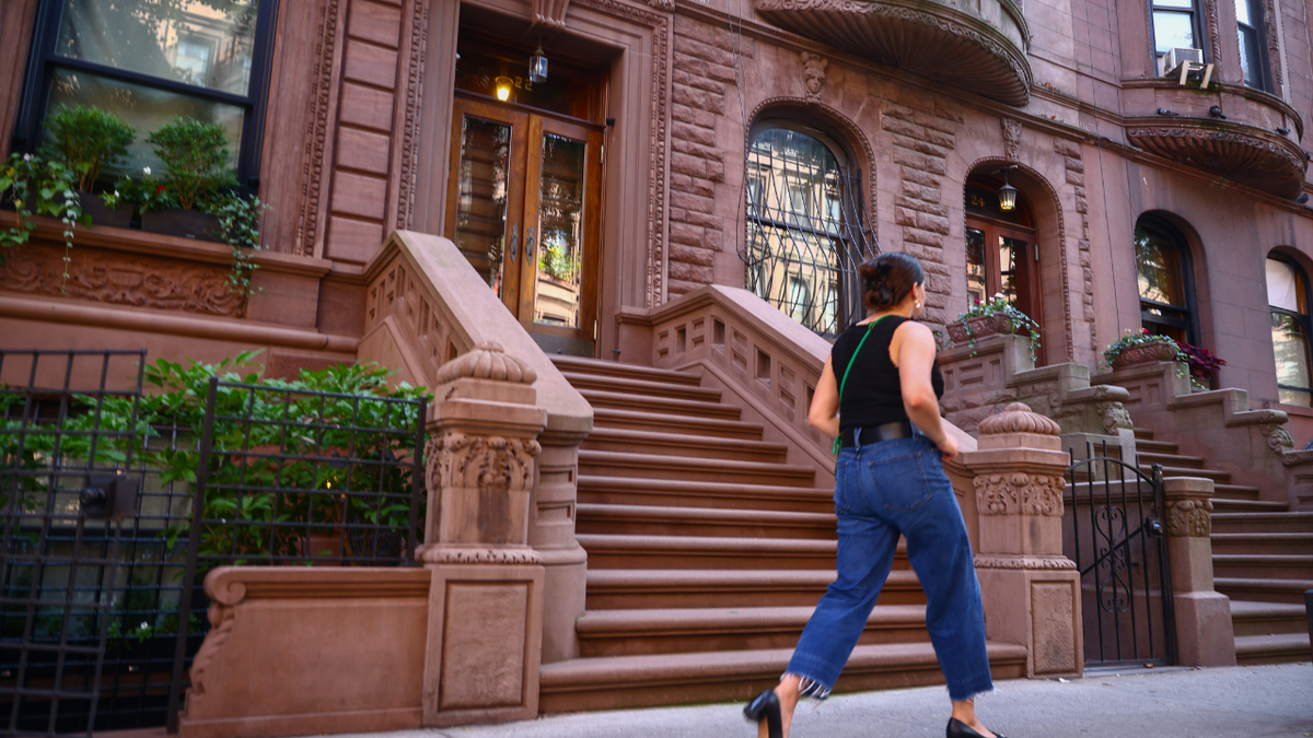 Una mujer camina frente a una hilera de edificios de piedra rojiza en Nueva York.