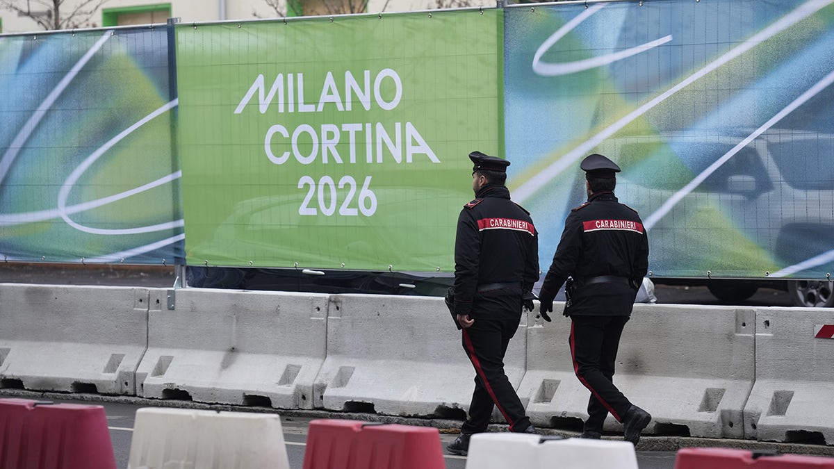 Police walk by a Milan Cortina banner
