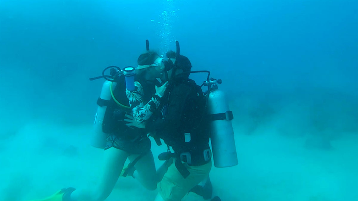 Scuba diving couple kissing underwater after romantic ocean proposal.