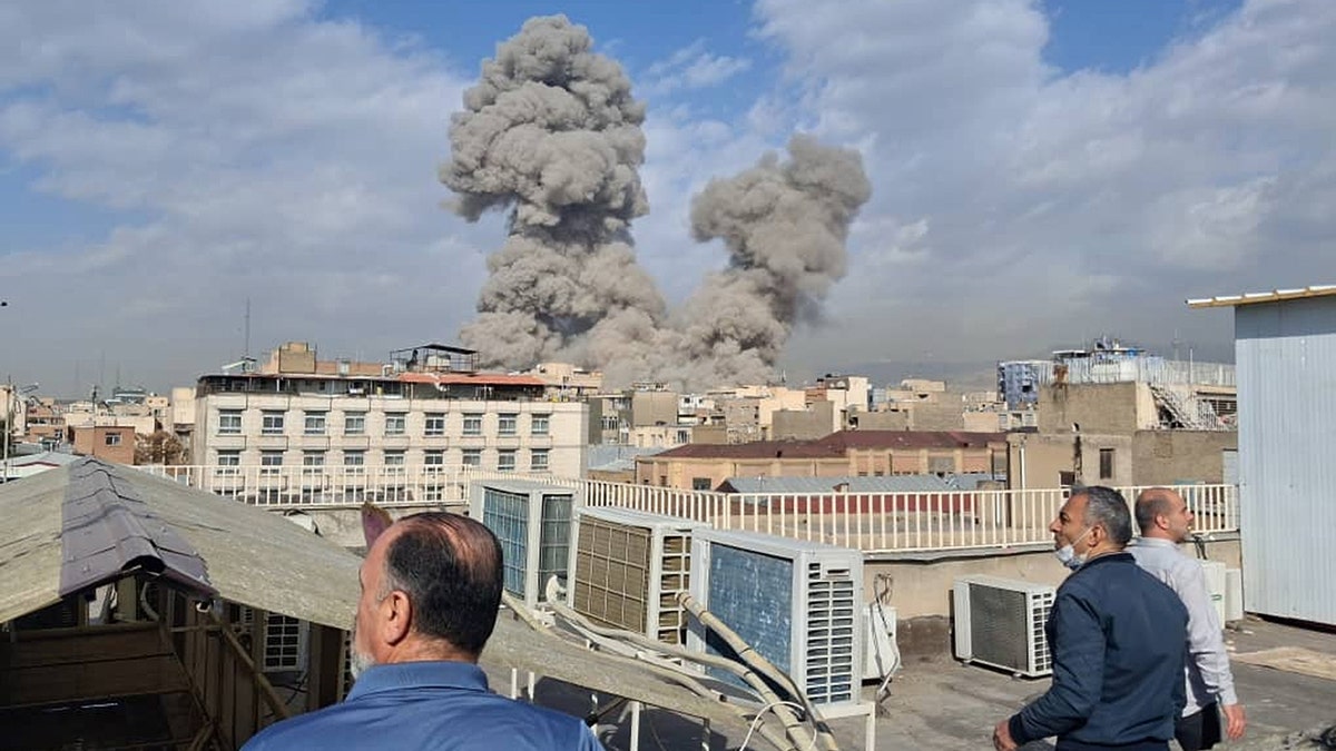 People watch smoke rise over rooftops in Iran