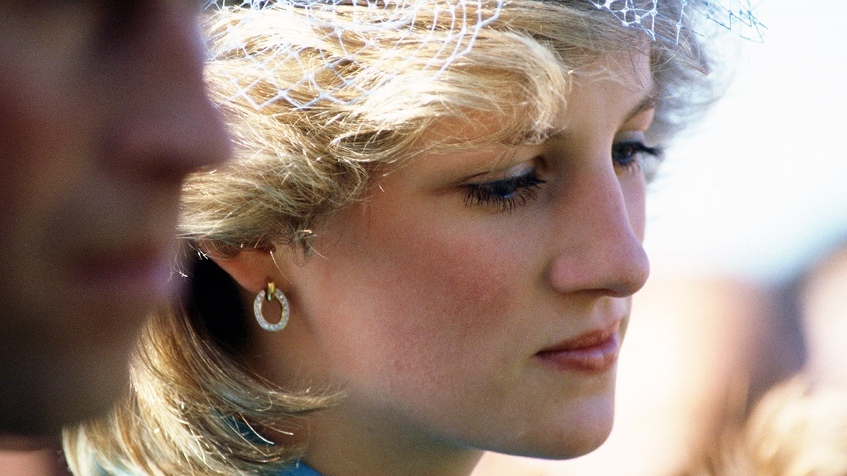 A close-up of Princess Diana looking somber in a lace fascinator.