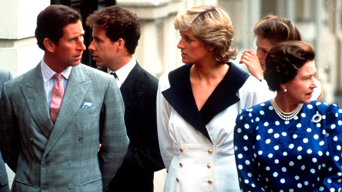 Prince Charles and Princess Diana having a serious conversation as they walk next to Queen Elizabeth who is wearing a bright blue polka dot dress.