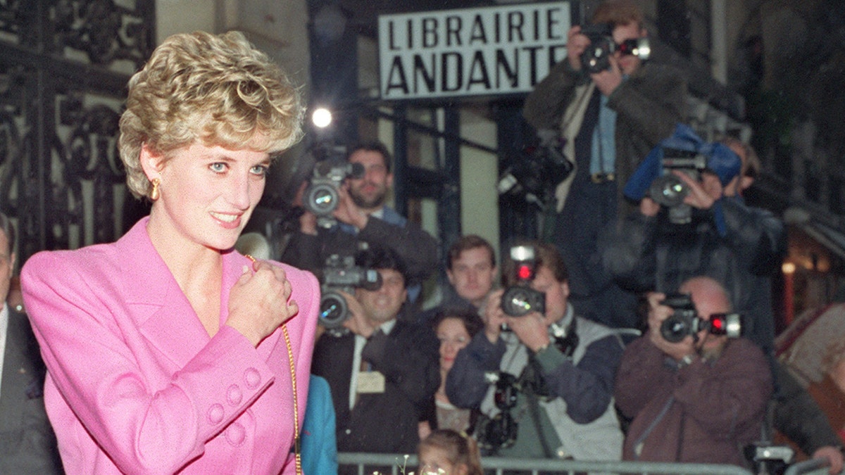 Princess Diana in a pink suit being photographed by paparazzi.