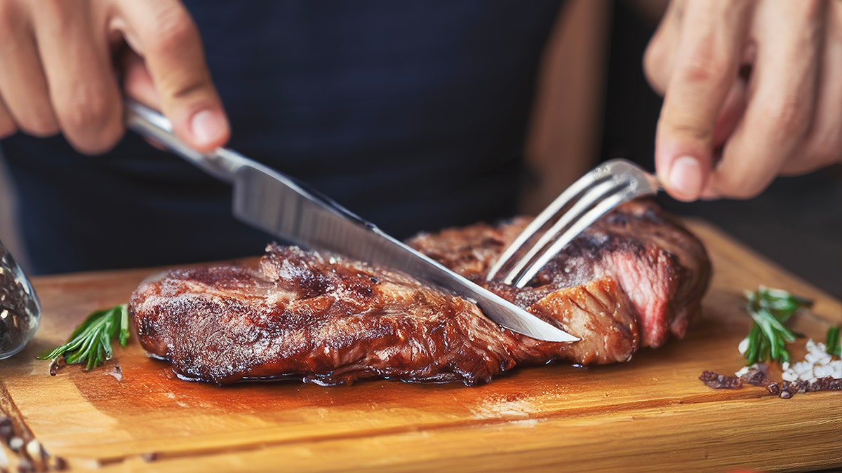 Person's hands seen cutting steak on cutting board.