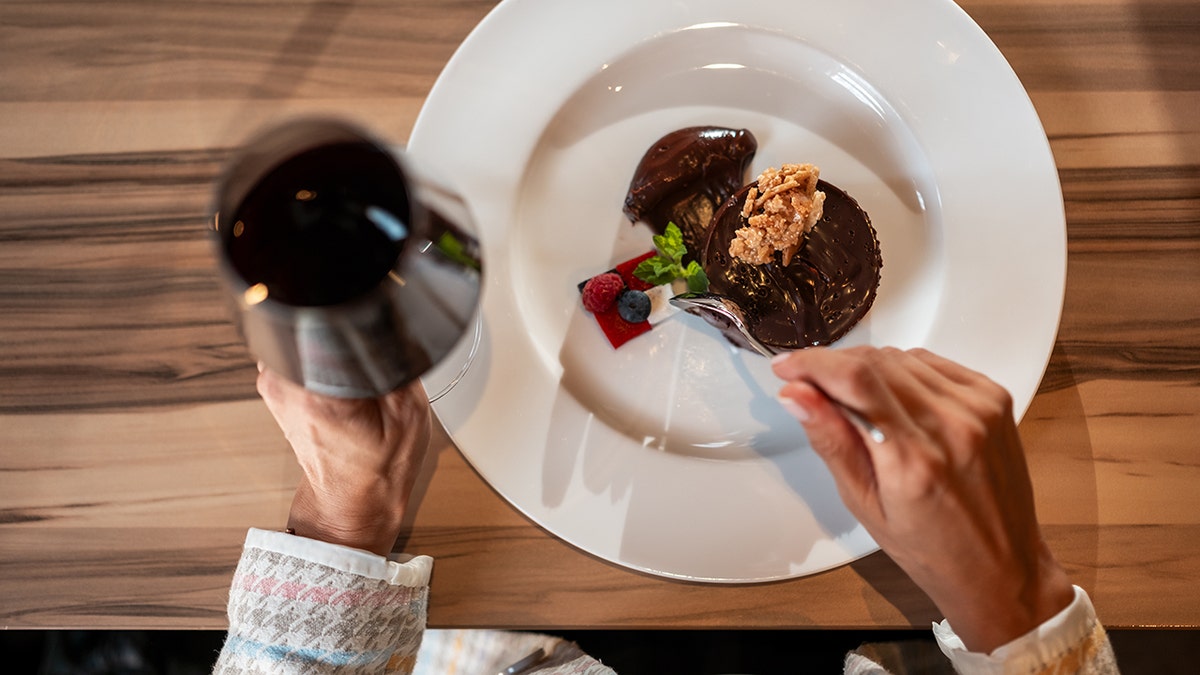 Elegant close-up of a rich chocolate dessert garnished with berries and mint, served with red wine in upscale restaurant.