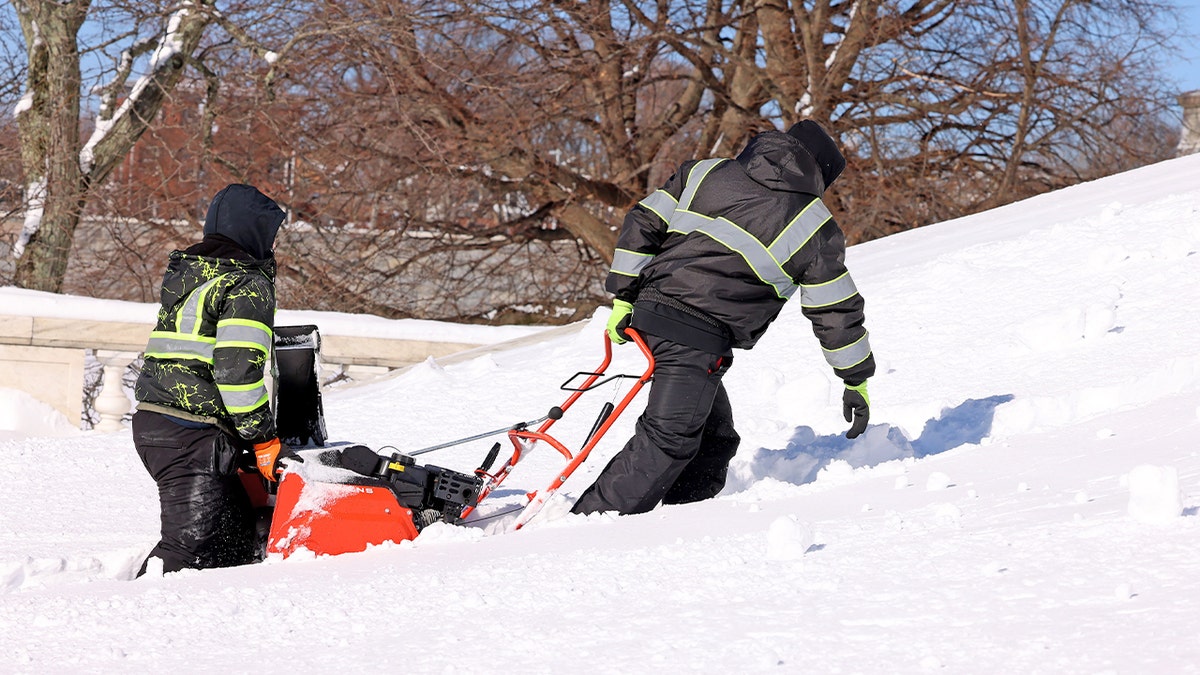 Two workers haul a snowblower up the steps of the Rhode Island State House after a major snowfall.