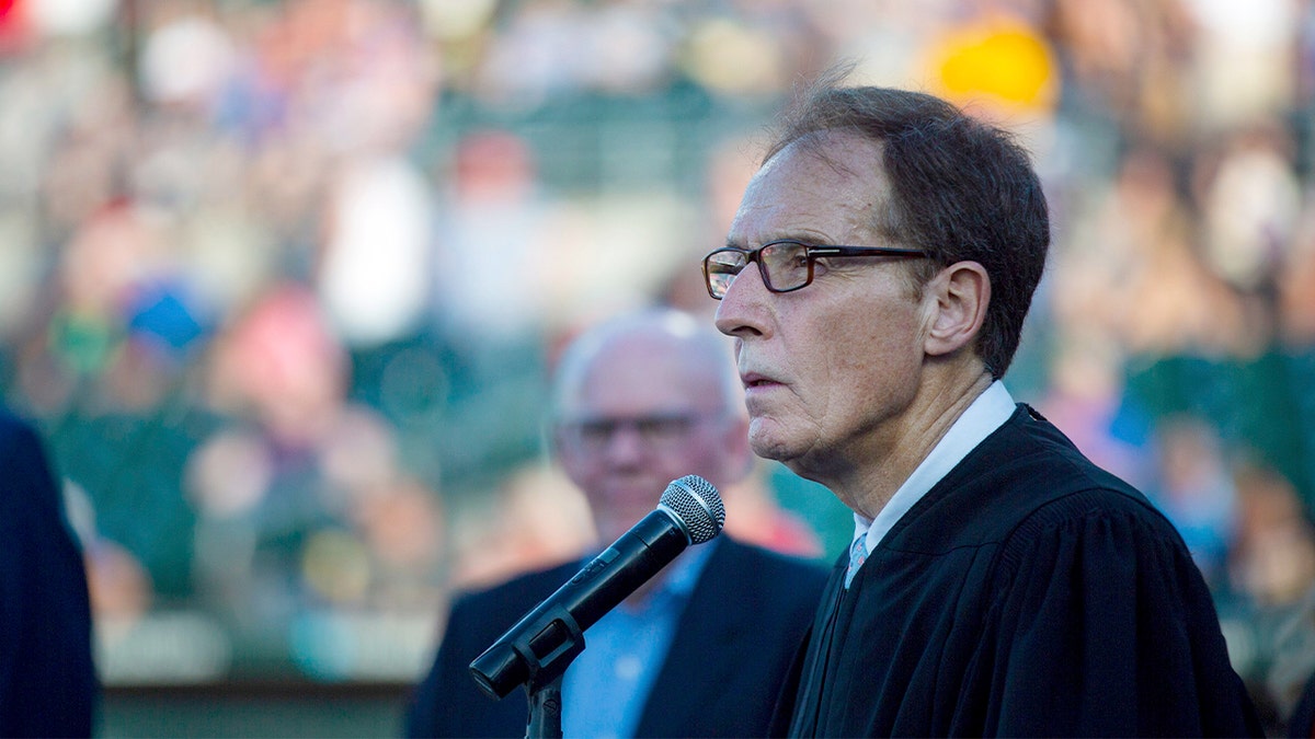 At a civic event, a judge stood on a podium at a baseball field and addressed the crowd.