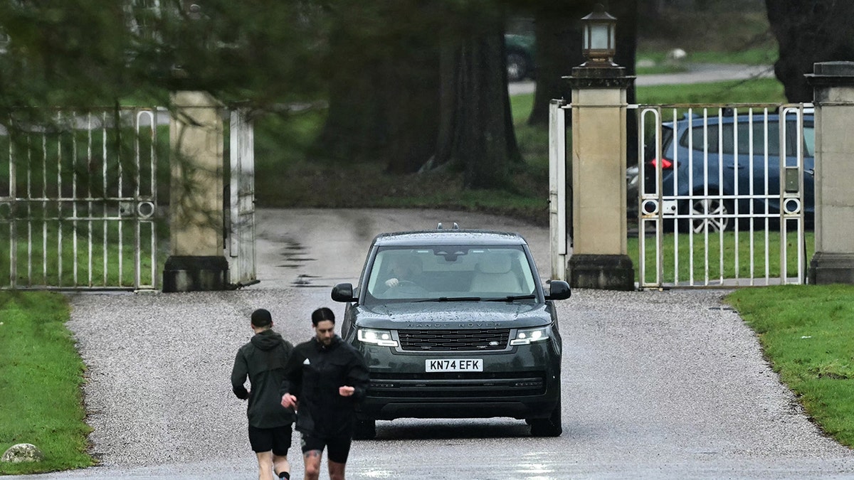 Two joggers in front of a car in front of Royal Lodge where Andrew Mountbatten-Windsor resides.