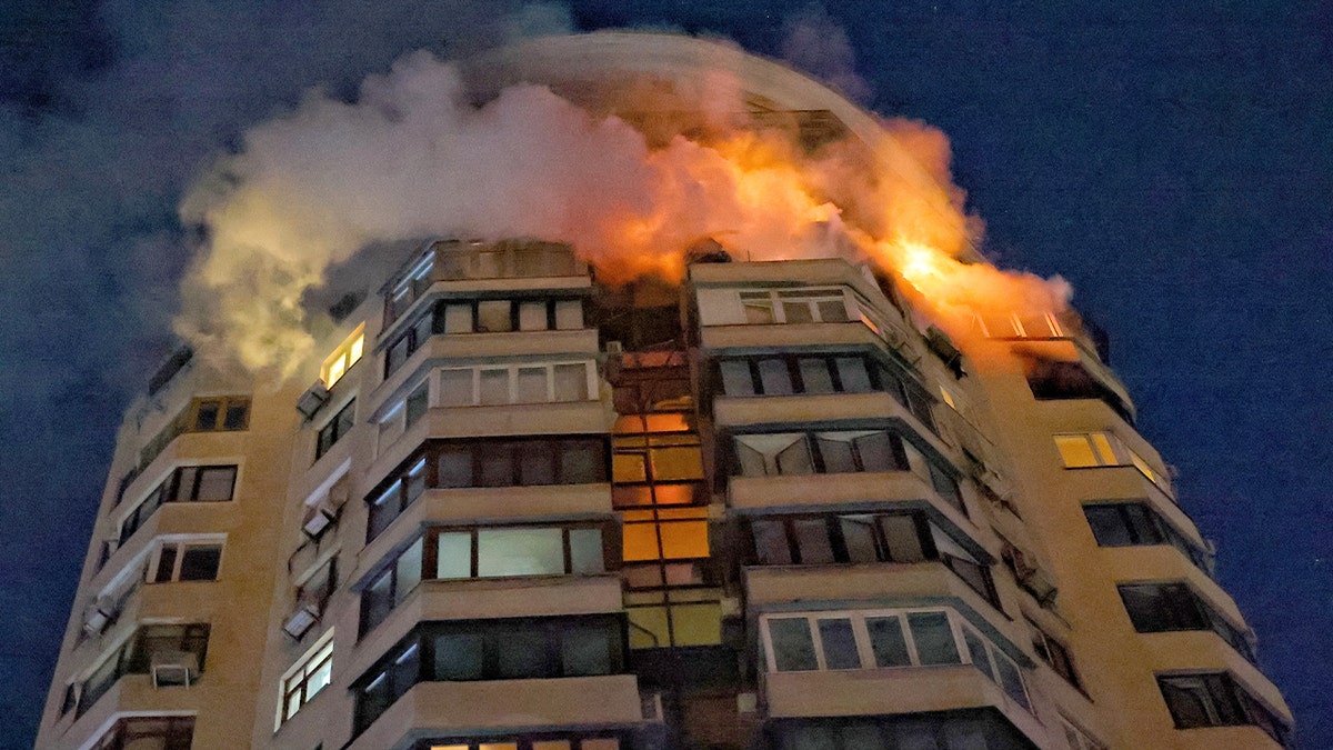 Flames rise from the upper floors of a high-rise building against the night sky in a residential area.