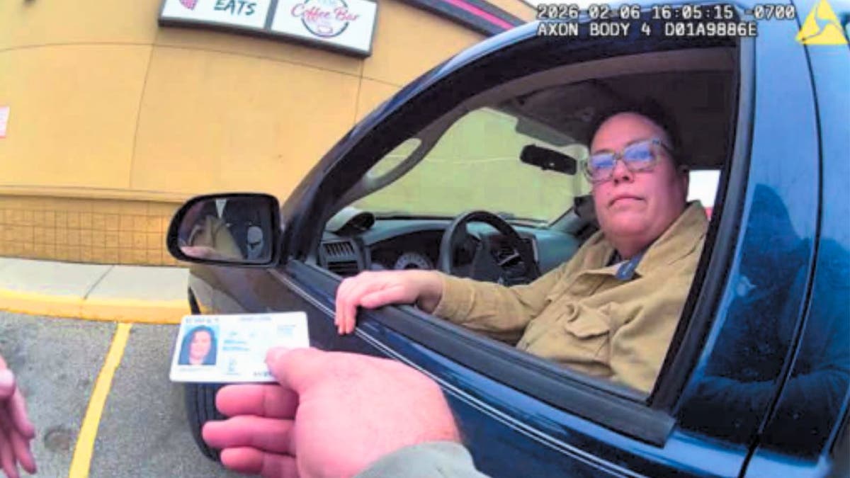 Woman seated in a blue pickup truck handing over an Idaho driver’s license during a traffic stop.