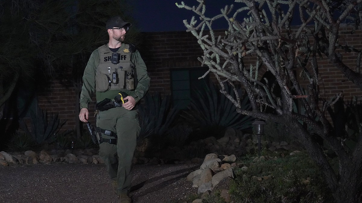 A member of the Pima County Sheriff's office standing on a residential street near Nancy Guthrie's house.
