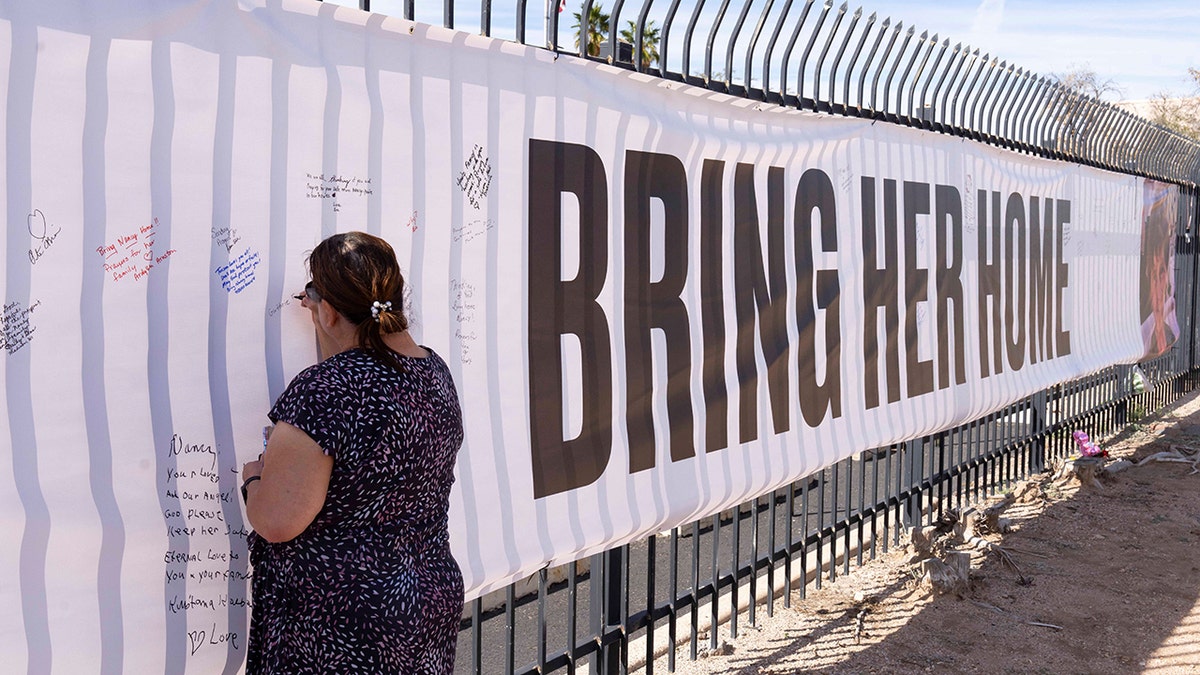 A well-wisher signing a banner with a photo of Nancy Guthrie outside KVOA newsroom in Tucson
