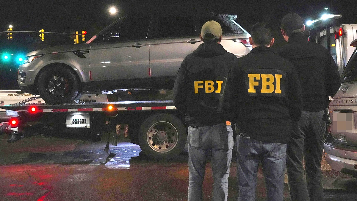 Agentes do FBI e delegados do xerife do condado de Pima, trabalhando no caso Nancy Guthrie, processando evidências de um Range Rover cinza em um estacionamento.