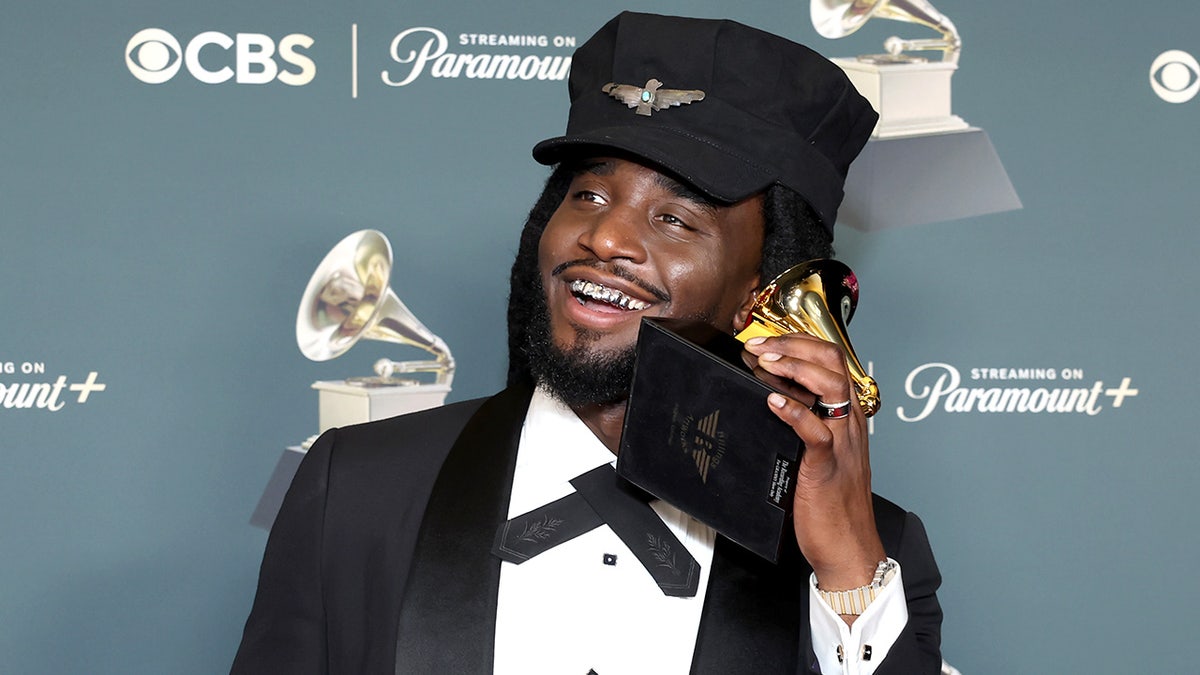 Shaboozey poses while holding an award in the press room at an awards ceremony.
