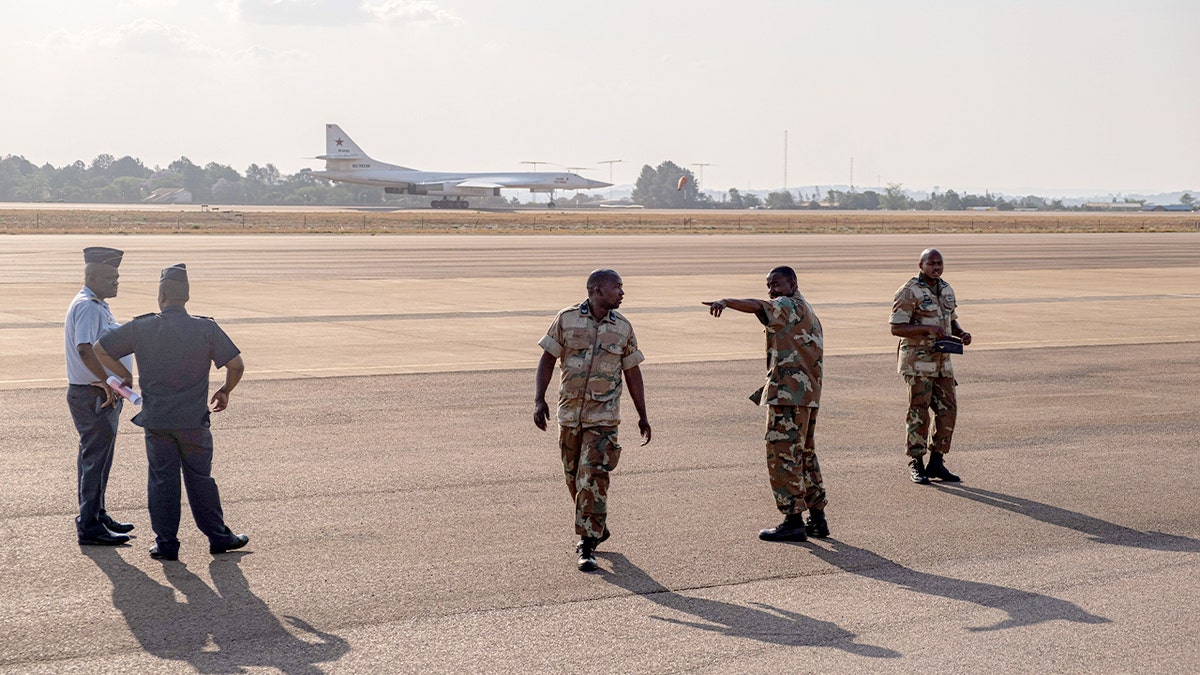 Police officers and soldiers stand on a runway as a large Russian military bomber touches down at an air base near Pretoria.