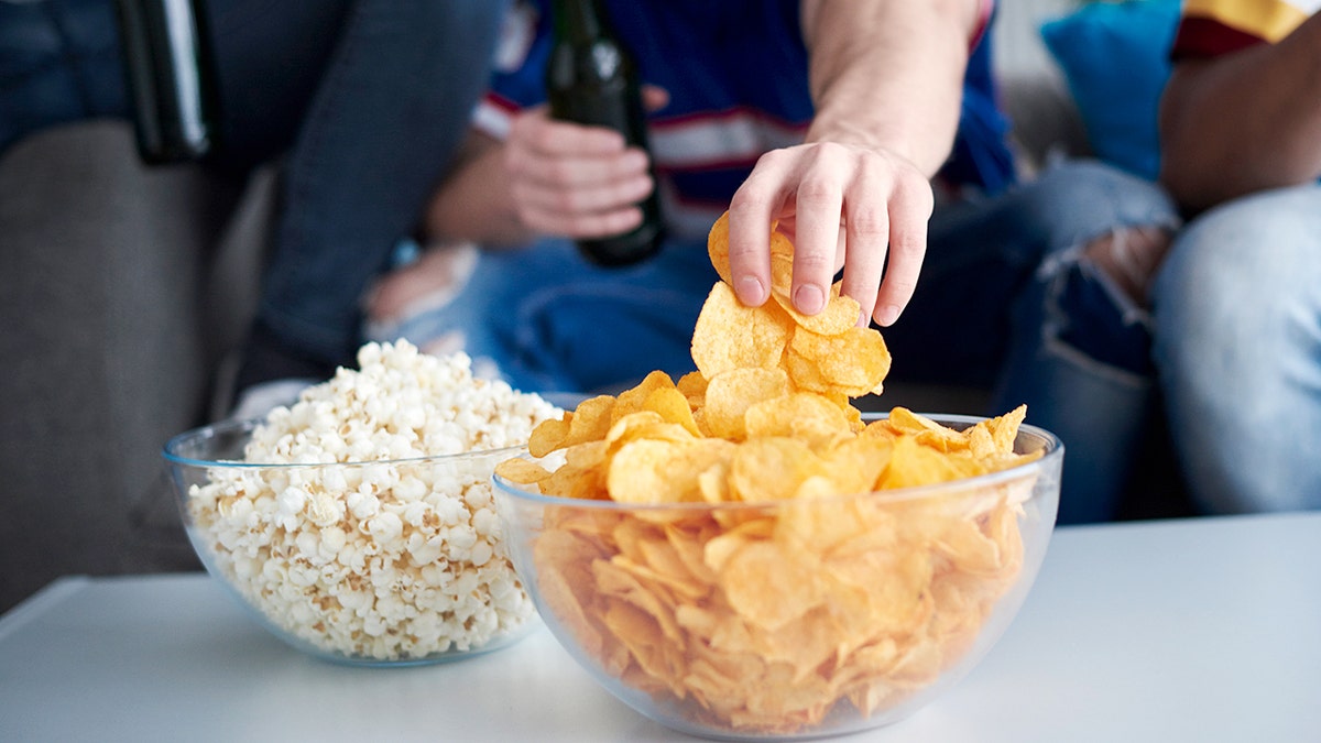 A man's hand reaches for chips in a bowl during a Super Bowl party.