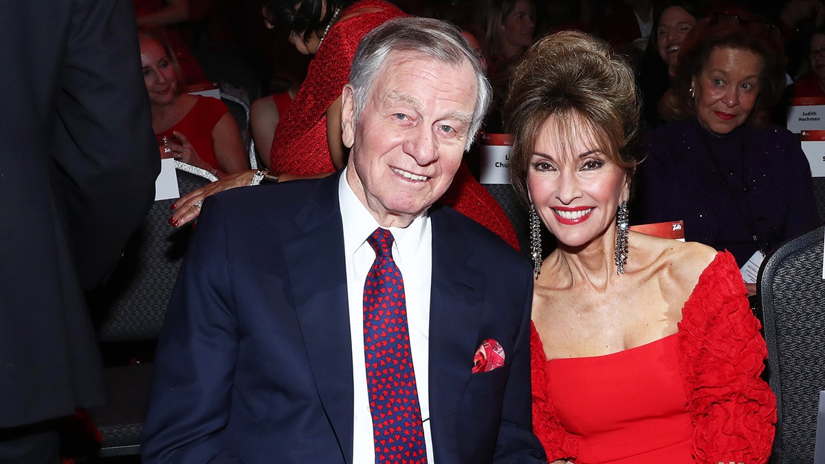 Helmut Huber wearing a dark suit with a blue and red tie sitting next to Susan Lucci in a red dress.