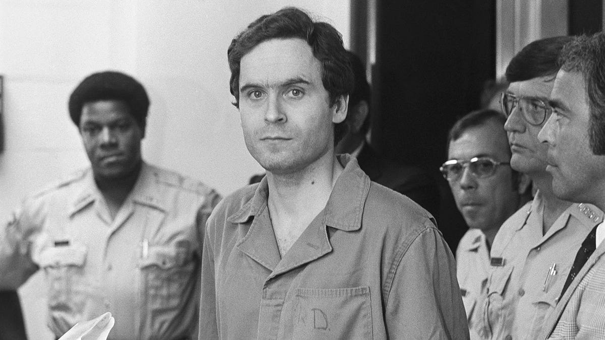 Ted Bundy in a jumpsuit looking serious in front of the camera.