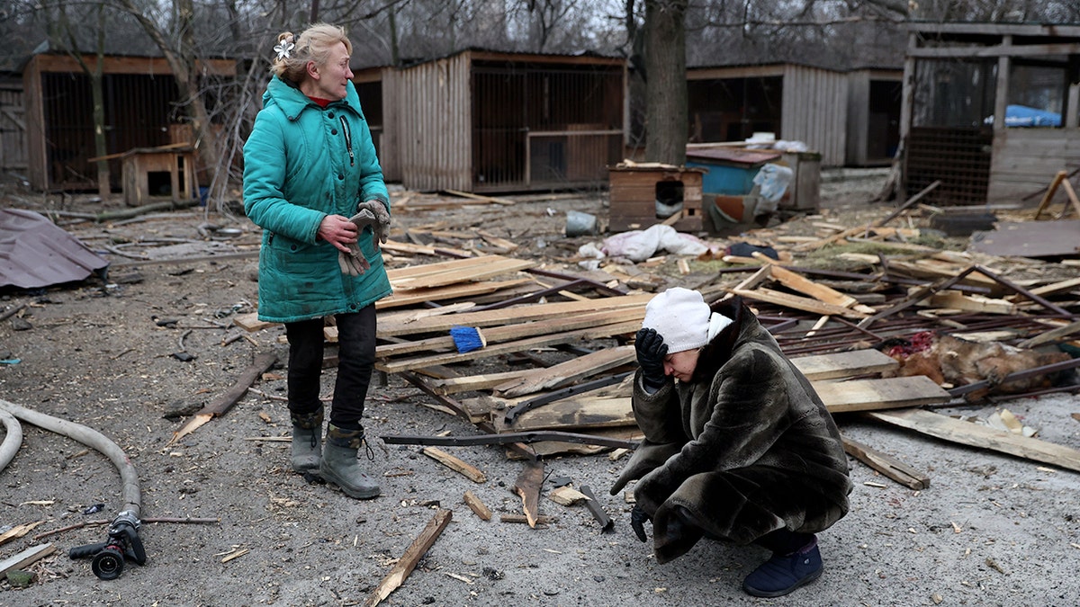 A woman stands while another kneels in front of ruins after a Russian strike in Ukraine
