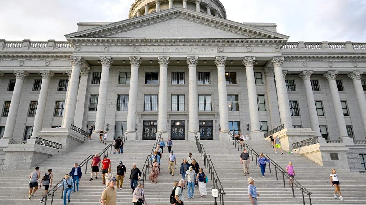 Visitors walk and gather on the grounds of a domed state capitol building.