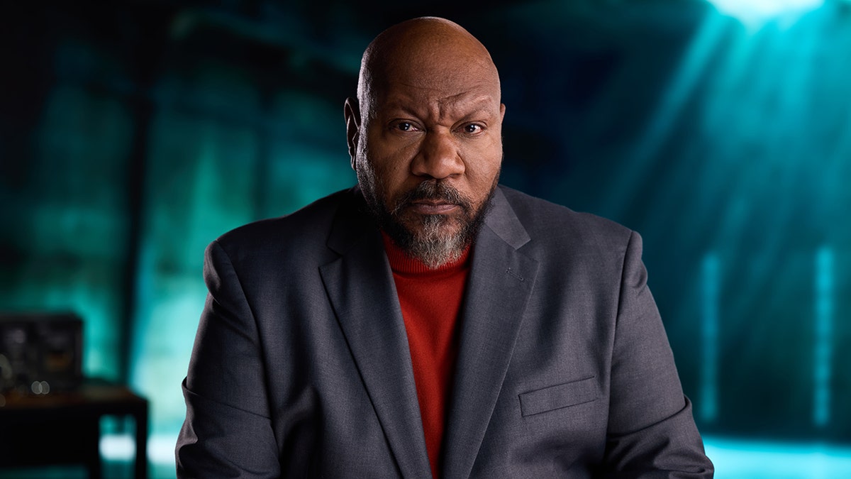 Ving Rhames in a dark grey suit and a red shirt.