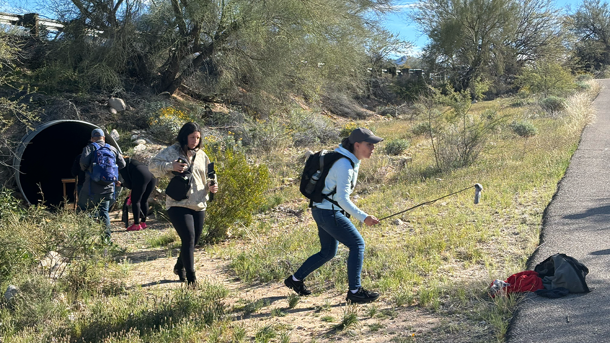 A woman moves discarded clothing with a walking stick in the search for Nancy Guthrie.