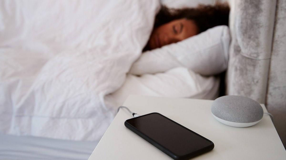 Woman Asleep In Bed With Mobile Phone And Voice Assistant On Bedside Table