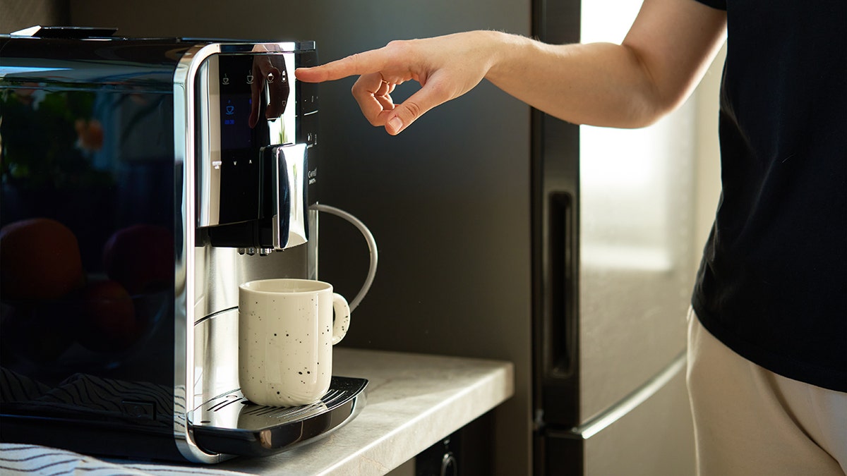 Person pressing button on automatic coffee machine with mug underneath.