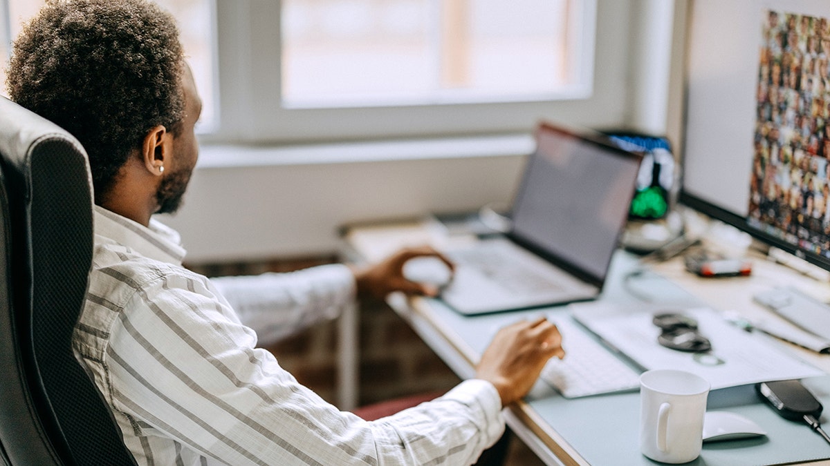 Young businessman using a laptop and looking at computer monitor at his desk