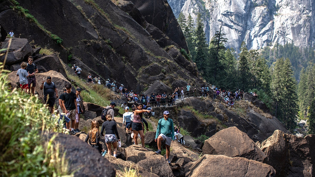 Crowded hiking trail in California with visitors climbing over large rocks in a forested mountain valley with granite cliffs.
