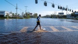 A person wading through knee-deep water on a flooded residential street in Florida.