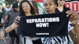 People holding signs supporting reparations
